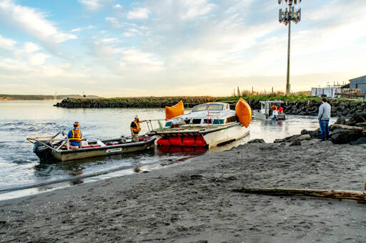 Port of Port Townsend Harbormaster Kristian Ferrero, right, watches as a crew from Seattle Global Diving and Salvage work to remove a derelict catamaran that was stuck in the sand for weeks on a beach at the Water Front Inn on Washington Street in Port Townsend. The boat had been sunk off of Indian Point for weeks before a series of storms pushed it to this beach last week. (Steve Mullensky/for Peninsula Daily News)