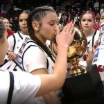 Neah Bays Qwaapeys Greene holds the girls basketball state championship trophy as her teammates celebrate its fourth straight title early Sunday morning in Spokane. (NFHS Network)