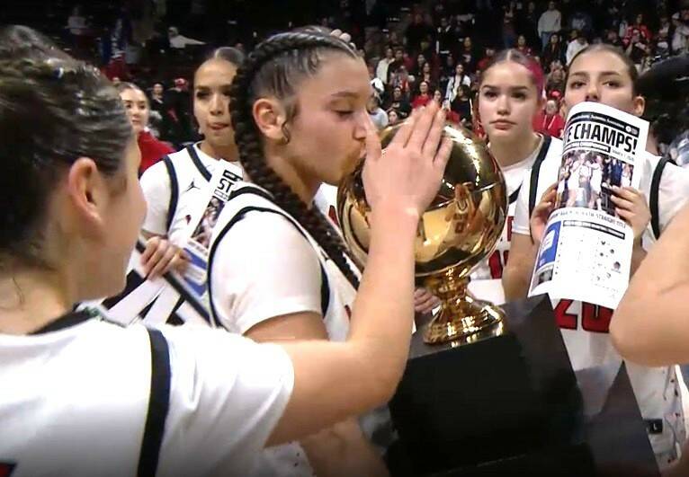 Neah Bays Qwaapeys Greene holds the girls basketball state championship trophy as her teammates celebrate its fourth straight title early Sunday morning in Spokane. (NFHS Network)