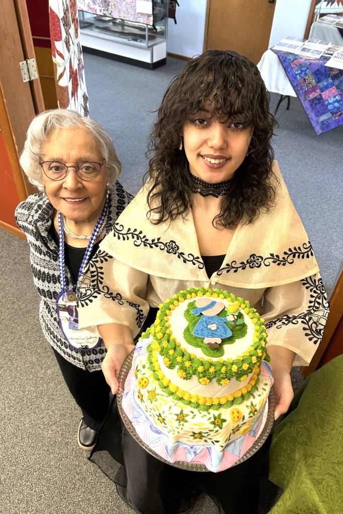 Sage Glover, the Sunbonnet Sue Quilt Clubs youngest member, holds a cake she made for the clubs 40th anniversary party on April 8. She stands by her grandmother Martha Scott, another longtime club member, who purchased the ingredients for the cake. (Matthew Nash/Olympic Peninsula News Group)