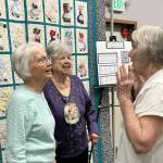 Longtime Sunbonnet Sue Quilt Club members, from left, Nancy Davis, Alicia Crawford and Joanne Thoma share a story during the club’s 40th anniversary party. They’re standing by the “Sunbonnet Sue Friendship Quilt” that was one of a handful of quilts on display. (Matthew Nash/Olympic Peninsula News Group)