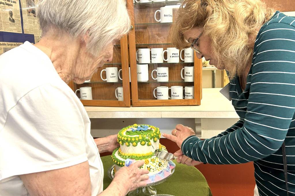 The Sunbonnet Sue Quilt Clubs most tenured member, Joanne Thoma, left, works with its newest, Stephannie Flynn, who joined two weeks ago, to cut a special cake made by the clubs youngest member, Sage Glover. Flynn said she moved to the area two years ago and wanted to be more active in the community and connected with the club through her neighbor Toni Cline. (Matthew Nash/Olympic Peninsula News Group)