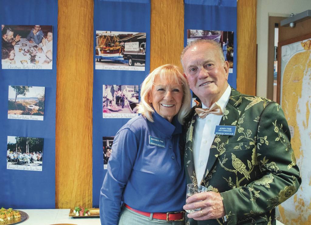 Marian and Jerry Fine, vice commodore of the Sequim Bay Yacht Club, pause before a display of images from the early days of the club during the 50th anniversary celebration at John Wayne Marina. (Emily Matthiessen/for Olympic Peninsula News Group)