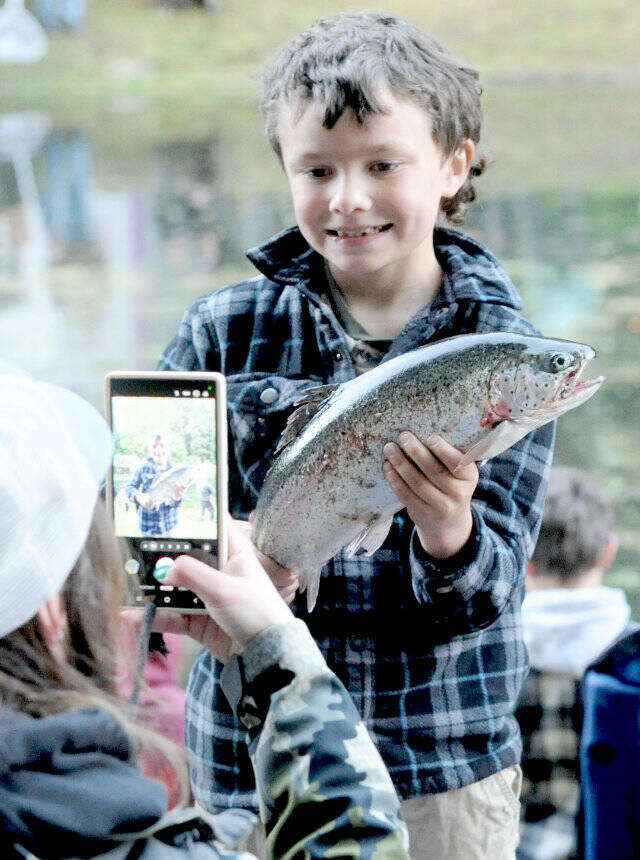 Aaron Peterson, 7, displays his catch for his mother during the annual Kids Fishing Day held at the Washington Department of Fish and Wildlifes Bogachiel Hatchery in Forks. There was plenty of sunshine, fishermen and trout, along with the serving of hot dogs, donuts and hot chocolate by the Forks Elks Club. The annual derby is sponsored by the West End Sportsmens Club along with many other donors and volunteers. (Lonnie Archibald/for Peninsula Daily News)