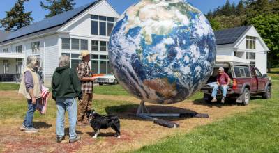 Park visitors look at a huge inflatable globe that was on display in the Commons at Fort Worden State Park for Global Earth Repair Convergence through Monday. The globe is the work of Eric James Morris of Orcas Island, sitting on the tailgate, who has been making globes for more than 40 years. The convergence had a number of workshops, panels, vendors and music over a five-day period to help bring the world together and to heal and cool the planet. (Steve Mullensky/for Peninsula Daily News)