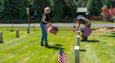 Alysa Thomas, left, and Dean Bartl, both from Port Townsend and employees of Tessera, a facilities management company, place American flags on the graves at the Fort Worden Military Cemetery on Friday, in advance of todays Memorial Day services. (Steve Mullensky/for Peninsula Daily News)