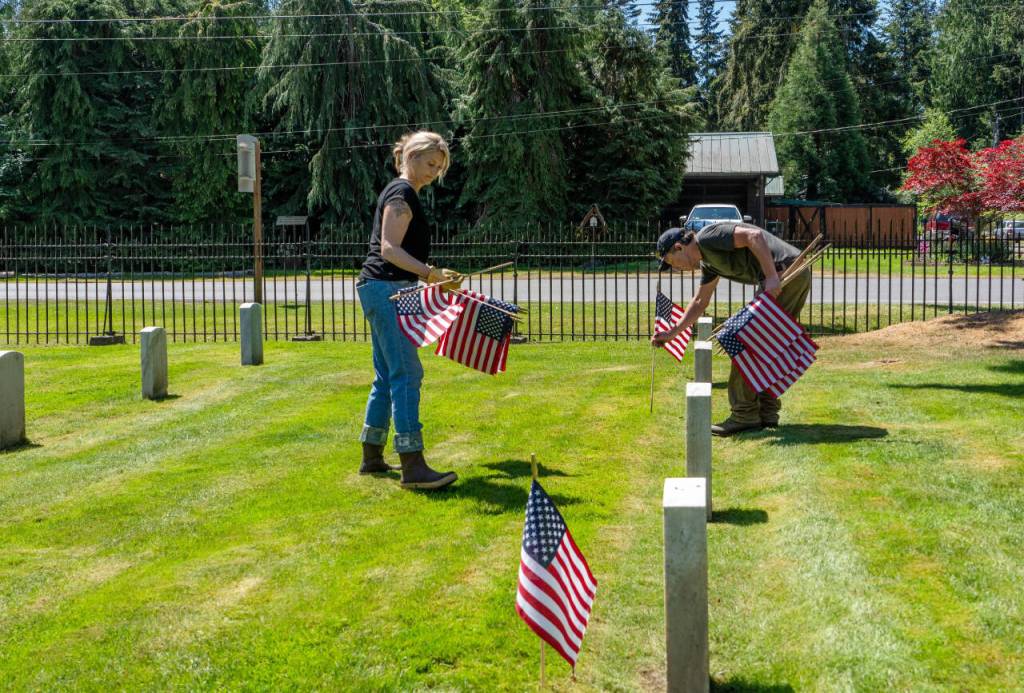 Alysa Thomas, left, and Dean Bartl, both from Port Townsend and employees of Tessera, a facilities management company, place American flags on the graves at the Fort Worden Military Cemetery on Friday, in advance of todays Memorial Day services. (Steve Mullensky/for Peninsula Daily News)