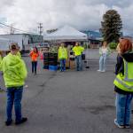 Virginia Reitsma, left, in orange shirt, director of administration and coordinator of the Sequim Food Banks Teen Program, holds a brief huddle with a group of young volunteers just prior to the 9 a.m. start of the drive-through food distribution line on a recent Saturday. The Teen Program currently has a roster of 50, Reitsma said. Although there is adult supervision, the teens manage the entire food distribution operation every Saturday. (Emily Matthiessen/Olympic Peninsula News Group)
