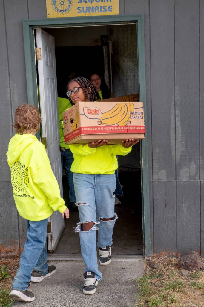 Kaysin Gluth passes fellow Sequim Food Bank youth volunteer Trinity McNorris as she carries a box of food from storage to an outdoor food station. (Emily Matthiessen/Olympic Peninsula News Group)