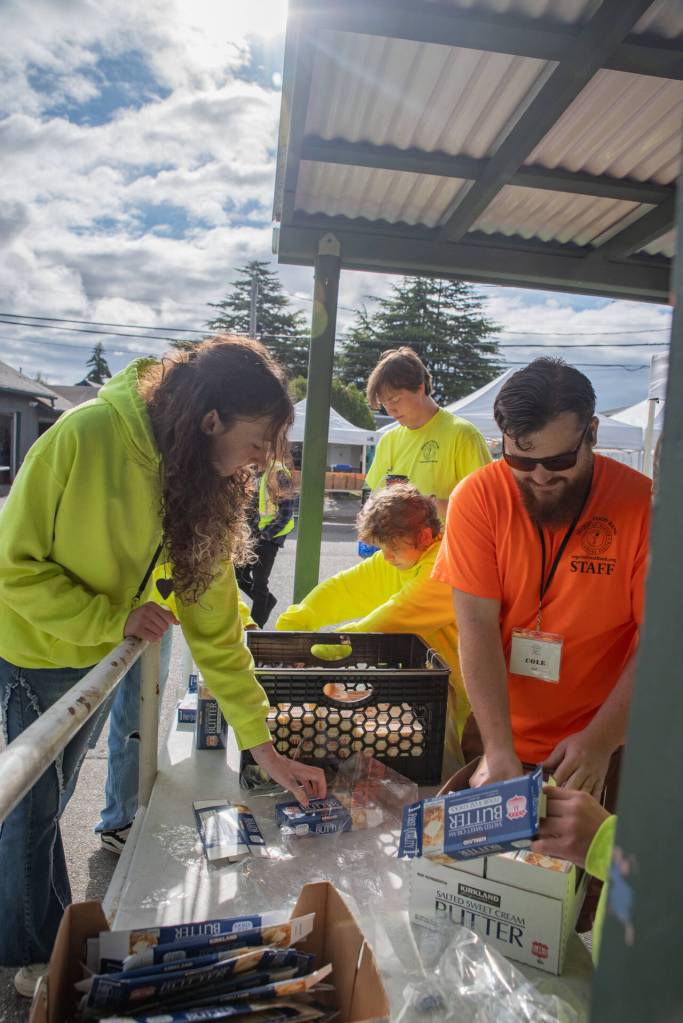 Sequim Food Bank Transportation and Saturday Distribution Coordinator Cole Tierney, in orange shirt, works with students in preparation for three hours of food distribution on a recent Saturday. In the background, in a yellow shirt, is Brayden Baritelle, 15, who was 13 when he became the youngest volunteer to receive the food banks Junior Volunteer of the Year Award. He was recently among the first to receive a Youth Award as part of the annual Clallam County Community Service Awards. (Emily Matthiessen/Olympic Peninsula News Group)