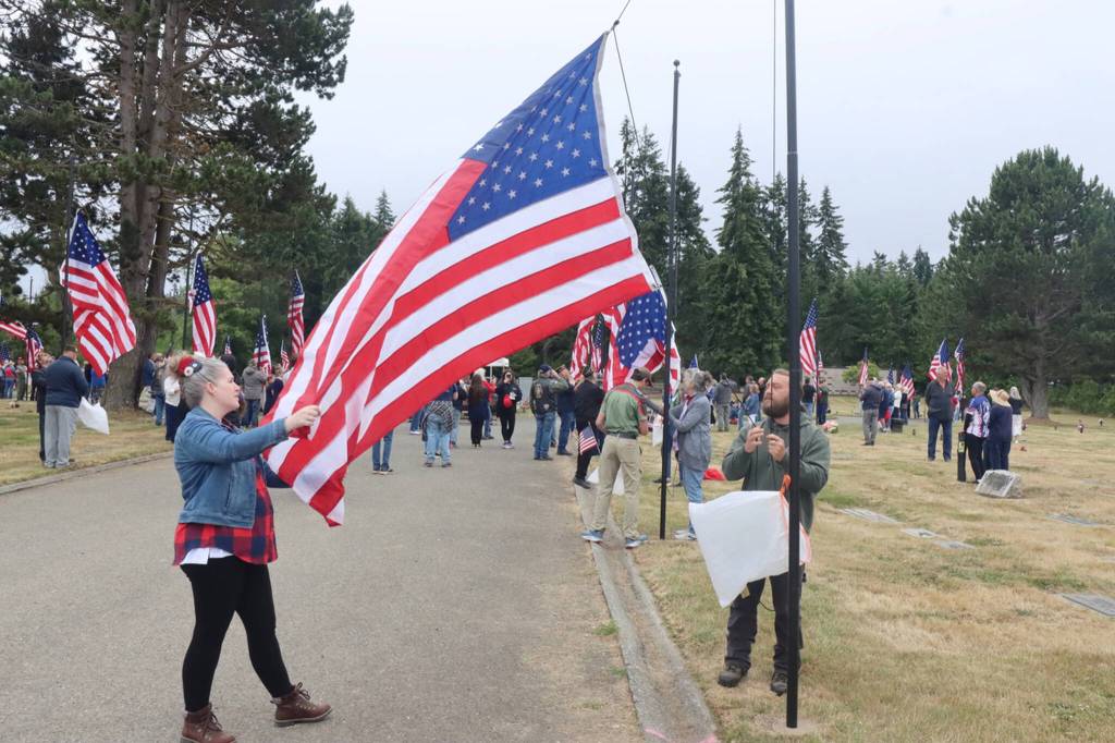 Volunteers Emily and Zach Batton of Sequim unfurl and raise one of the new 50 flags raised on Saturday at at the Mount Angeles Memorial Park Cemetery. More than a hundred people attended the special event, a project of the Carlsborg VFW and the Michael Trebert chapter of the Daughters of the American Revolution. (Dave Logan/for Peninsula Daily News)