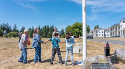 Mike Howard, left, and his wife Carol, from Sequim, and their grandkids, Graham and Abbie, from Sacramento, pull on the lanyard to raise the American flag on the new flagpole during a ceremony on Wednesday at Fort Worden State Park. The previous flagpole was more than 100 years old and made of wood, and it blew over during a windstorm last year, barely missing the Howards as they were walking toward the ranger office. Months later, Mike Howard realized he missed seeing the pole, so he and Carol donated $3,000 to purchase a replacement. The Friends of Fort Worden contributed the remaining funds to make the purchase complete. The new pole is 40 feet tall and made of fiberglass. (Steve Mullensky/for Peninsula Daily News)