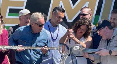 Peninsula College President Suzy Ames, right, cuts a metal ribbon to celebrate the launch of the schools Mobile Workforce Program and a new 53-foot-long trailer outfitted with eight welding booths that is designed to bring job training across the North Olympic Peninsula. Among those attending the event were former State Sen. Steve Tharinger, left, and college trustee Glenn Ellis Jr., center. (Paula Hunt/Peninsula Daily News)