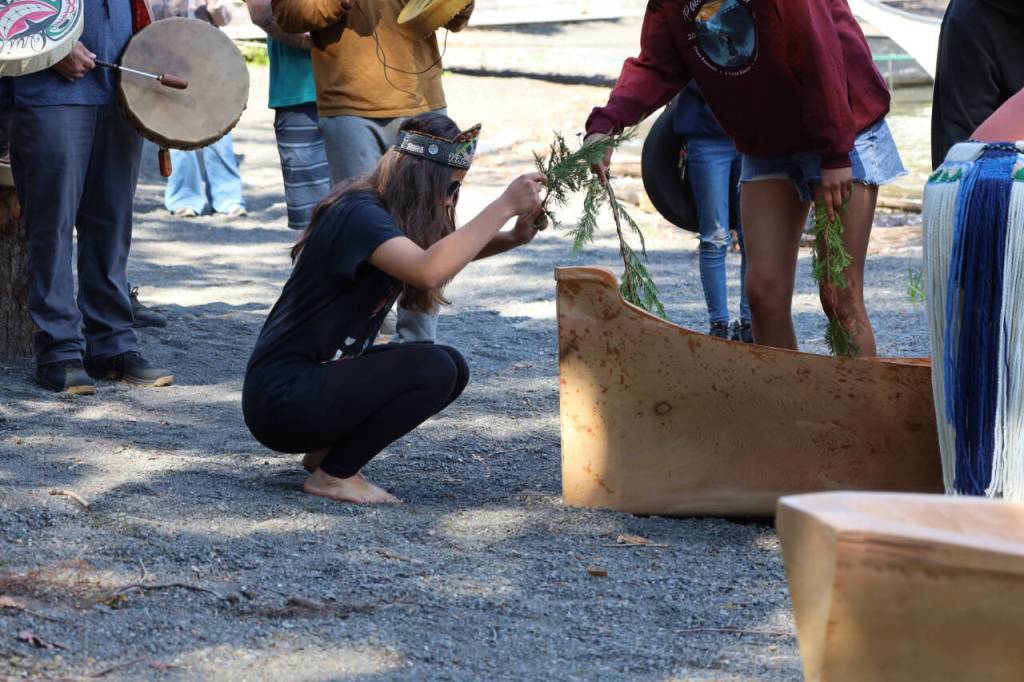 Valerie Charles blesses a canoe with a cedar branch dipped in Lake Crescent on Thursday at the NatureBridge Campus. (Emily Hanson/Peninsula Daily News)